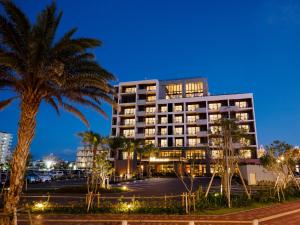 a building with a palm tree in front of a parking lot at MB GALLERY CHATAN by THE TERRACE HOTELS in Chatan