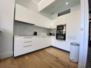 a white kitchen with white cabinets and a wooden floor at Le Téléphérique, vue Bastille, 6 pers, 300 m Gare in Grenoble