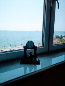 a clock sitting on a window sill with a view of the beach at Аппартаменты студия первая линия у моря в Совиньоне in Odesa