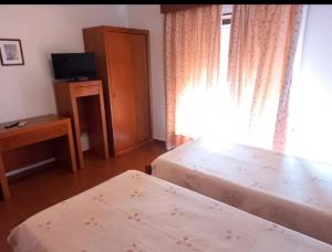 a bedroom with two beds and a television and a window at Hospedaria São João in Vidigueira