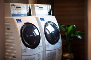 two washing machines are stacked next to a plant at Hotel Xcell 広島 流川通り in Hiroshima