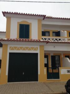 una casa gialla e bianca con un garage nero di A Casinha da Tita - Moradia com Terraço a Zambujeira do Mar