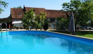 a blue swimming pool with an umbrella and a house at B&B Le Corbier in Herry