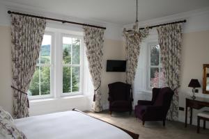 a bedroom with a bed and two chairs and windows at Arrandale House in Pitlochry