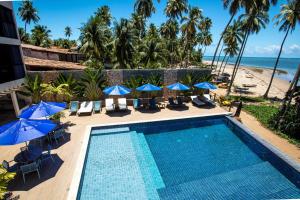 a swimming pool with umbrellas and chairs and the beach at CHOUPANA SUÍTES in Japaratinga