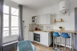 ベルサイユにあるLe Mousquetaireの白いキャビネットと青い椅子、窓付きのキッチン