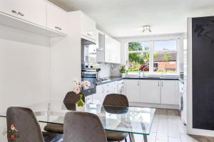 a white kitchen with a glass table and chairs at NIKSA Serviced Accommodation - 3 bedroom house in Welwyn Garden City