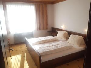 a bedroom with a bed with white sheets and a window at Gästehaus Bräuer in Neukirchen am Großvenediger