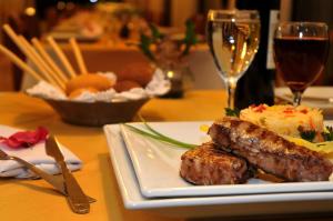 un plato de comida con carne y una copa de vino en Orquideas Hotel & Cabañas en Puerto Iguazú