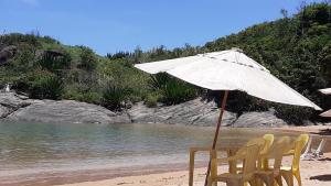 a table and chairs on a beach with an umbrella at Apartamento a Beira Mar em Setiba Guarapari in Guarapari