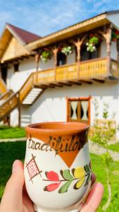 a person holding a coffee cup in front of a house at Pensiunea Casa Traditiilor in Ieud