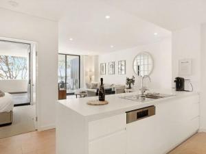 a white kitchen with a sink and a living room at 204 on the Beach by Experience Jervis Bay in Huskisson