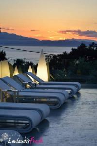 a row of blue lounge chairs in front of a sunset at Louloudis Fresh-Adults Only in Skala Rachoniou
