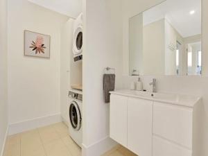 a white bathroom with a sink and a washing machine at Banksia on Blenheim by Experience Jervis Bay in Vincentia