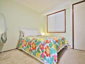 a bedroom with a bed with a colorful comforter and a window at Peace by the Beach by Experience Jervis Bay in Vincentia