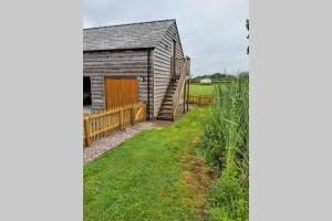 an old barn with a wooden fence next to a field at Swallows Retreat: A Country Loft Apartment in Hargrave