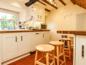 una cocina con armarios blancos y taburetes de madera en Lychgate Cottage, en Settle