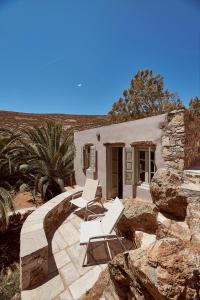 Deux chaises blanches et une maison avec des rochers dans l'établissement Nature Eco Living Serifos, à Livadiá