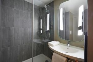 ein Bad mit einem Waschbecken und einer Dusche mit einem Spiegel in der Unterkunft ibis Archamps Porte de Genève in Archamps
