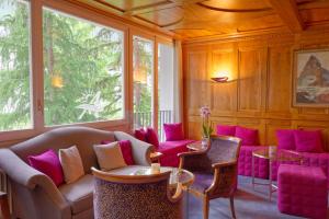 una stanza con sedie rosa, tavoli e finestre di Hotel Arca Solebad & Spa a Zermatt