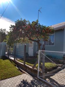 a fence in front of a house with a tree at CASA OTTON - Casa aconchegante, 3 quartos com cama de casal todos com ar condicionado in Gramado