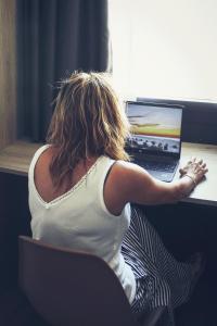 Hotel Mestral Perelló في بيريلو: امرأة تجلس في مكتب مع جهاز كمبيوتر محمول