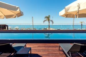 a swimming pool with chairs and umbrellas and the ocean at Dom Jose Beach Hotel (Plus) in Quarteira
