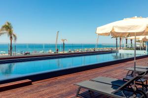 a swimming pool with chairs and an umbrella and the ocean at Dom Jose Beach Hotel (Plus) in Quarteira