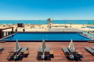 a swimming pool with chaise lounges and chairs next to the beach at Dom Jose Beach Hotel (Plus) in Quarteira