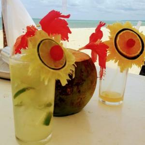 una mesa con dos cócteles y un coco y flores en Casa Porto Mar América Praia, en Porto Seguro