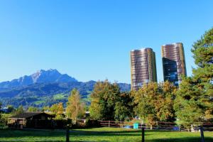 two tall buildings and trees with mountains in the background at HITrental Allmend Comfort Studios in Lucerne