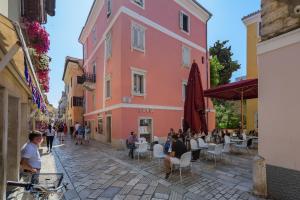a pink building with people sitting at tables in a street at Premium Apartment Daka in Poreč