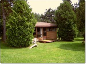 a small cabin with a porch in the grass at MacIver's Motel and Camp in Blind River