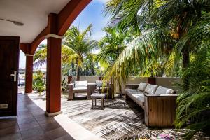 eine Terrasse mit einem Sofa, Stühlen und Palmen in der Unterkunft Chico's Seru Hulanda Resort in Willemstad