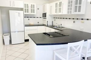 a white kitchen with a black counter and a refrigerator at Crystal Waters-2 bed, 2 bathroom, Beachfront Unit! in Bongaree