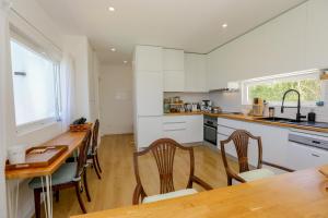 a kitchen with white cabinets and a wooden table and chairs at Like-home-T2 house, pool, AC, garden in Ericeira