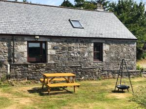 a wooden picnic table in front of a stone building at Anne's Cottage in Bargrennan