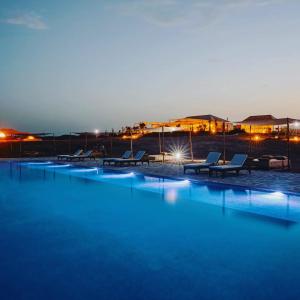 a large swimming pool with chairs and buildings at night at Oxygen Lodge Agafay in El Karia