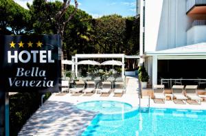 a hotel sign next to a swimming pool with chairs at Hotel Bella Venezia Mare in Lignano Sabbiadoro