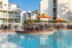 a swimming pool with chairs and umbrellas in a hotel at Ground floor, spacious patio and only steps away from beach and pool! in South Padre Island