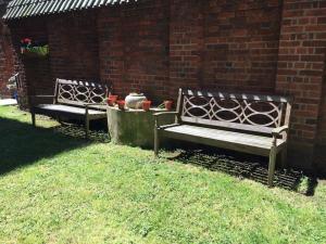 two benches sitting in the grass next to a brick wall at Marble Apartments Effra Court in London