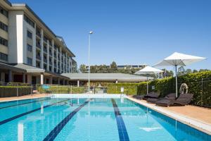 a swimming pool with chairs and umbrellas next to a building at Rydges Norwest Sydney in Baulkham Hills