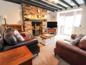 a living room with leather furniture and a stone fireplace at Capel Cottage in Penmaen-mawr