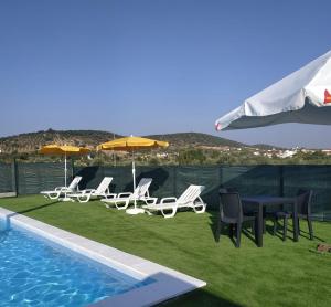 a group of chairs and tables and umbrellas next to a pool at Girassol Alojamento Local in Montemor-o-Novo