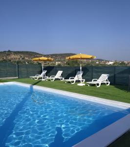 a swimming pool with two lawn chairs and umbrellas at Girassol Alojamento Local in Montemor-o-Novo