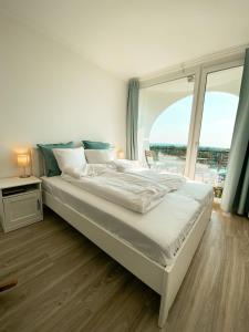 ein weißes Bett in einem Zimmer mit einem großen Fenster in der Unterkunft Marine Apartman By BLTN Siófok in Siófok