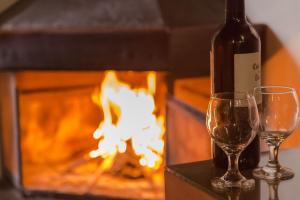 a bottle of wine and two glasses in front of a fireplace at Pousada D'lines in Campos do Jordão