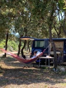 un hombre durmiendo en una hamaca junto a una furgoneta en Camping Sugar, en Mandre