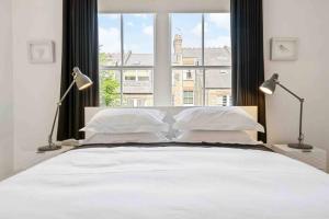 a white bed with two lamps and a large window at Luxury Apartment in Belsize Park in London