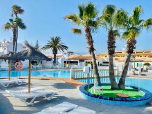 a resort pool with palm trees and lounge chairs at Happiness in Caleta De Fuste
